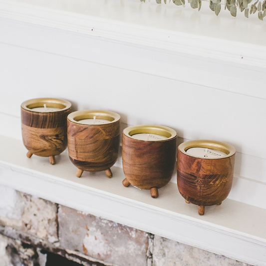 Set of four small footed teak wood candles with golden metal inserts on white mantel
